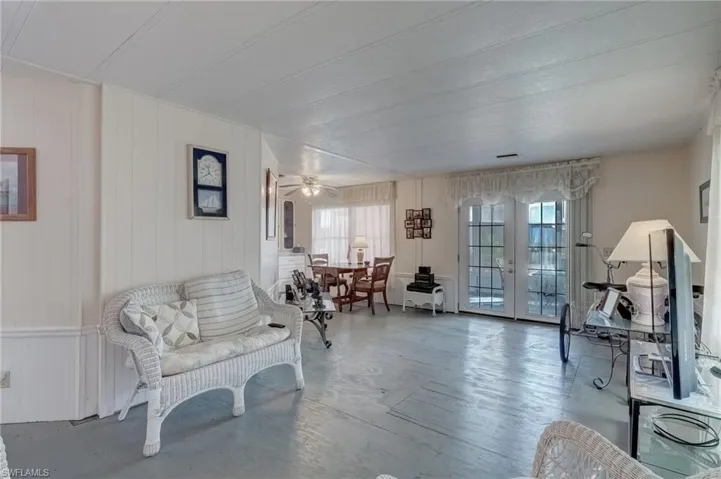 Sitting room featuring french doors, wooden walls, finished concrete floors, a ceiling fan, and a decorative wall