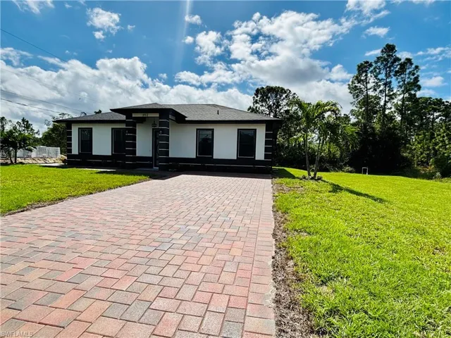 Prairie-style home with a front lawn, stucco siding, and decorative driveway