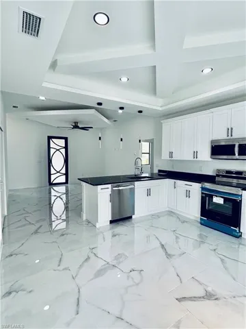 Kitchen featuring stainless steel appliances, white cabinets, a ceiling fan, light marble finish floors, and recessed lighting