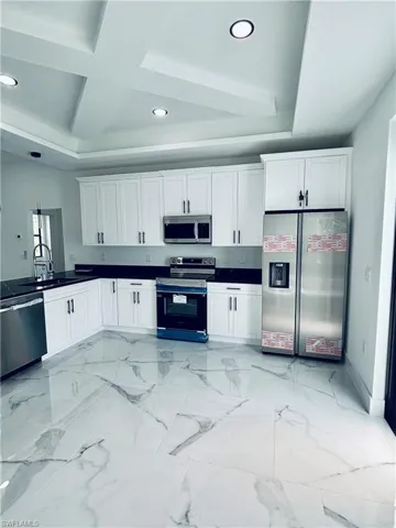 Kitchen featuring stainless steel appliances, white cabinets, recessed lighting, light marble finish flooring, and coffered ceiling