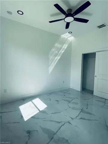Unfurnished bedroom featuring marble look tile flooring, ceiling fan, and a closet