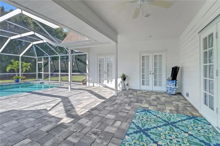 View of pool featuring glass enclosure, ceiling fan, a patio, and french doors