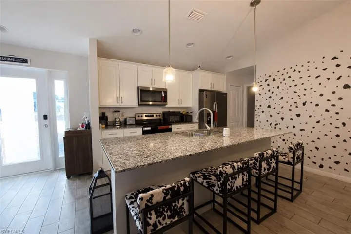 Kitchen featuring a kitchen bar, light stone counters, stainless steel appliances, decorative light fixtures, and a center island with sink