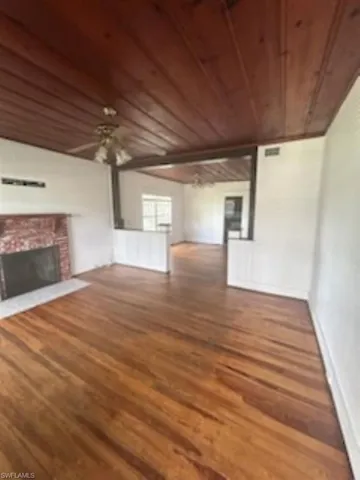 Unfurnished living room featuring wooden ceiling, wood finished floors, and a brick fireplace