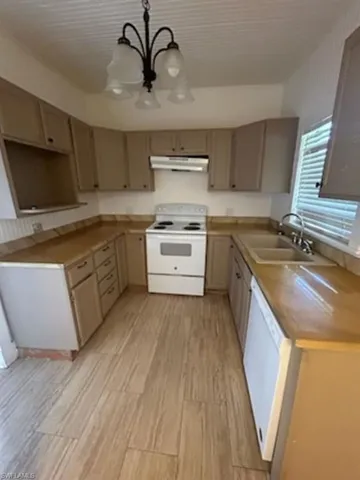 Kitchen featuring white appliances, under cabinet range hood, a chandelier, light wood-style floors, and hanging light fixtures