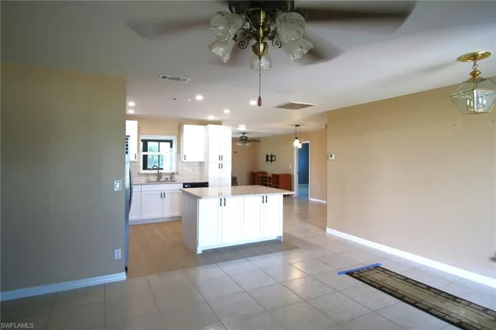 Kitchen with white cabinetry, decorative light fixtures, tasteful backsplash, ceiling fan, and light tile floors
