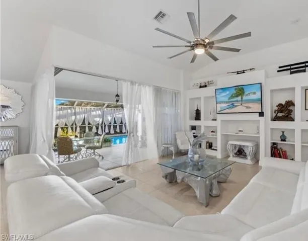 Tiled living room with built in features, a ceiling fan, and vaulted ceiling