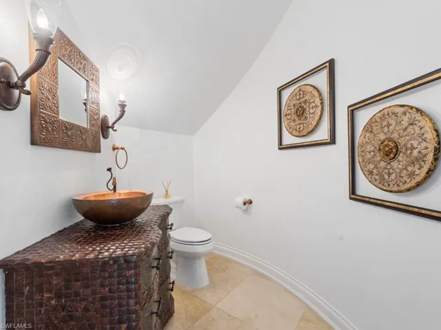 Bathroom featuring toilet, vanity, baseboards, and lofted ceiling