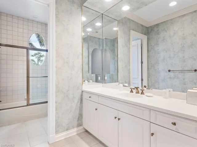 Full bathroom with baseboards, wallpapered walls, tile patterned floors, vanity, and shower / bath combination with glass door