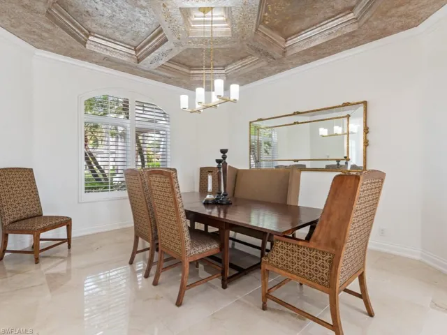 Dining area with baseboards, ornamental molding, coffered ceiling, and a notable chandelier