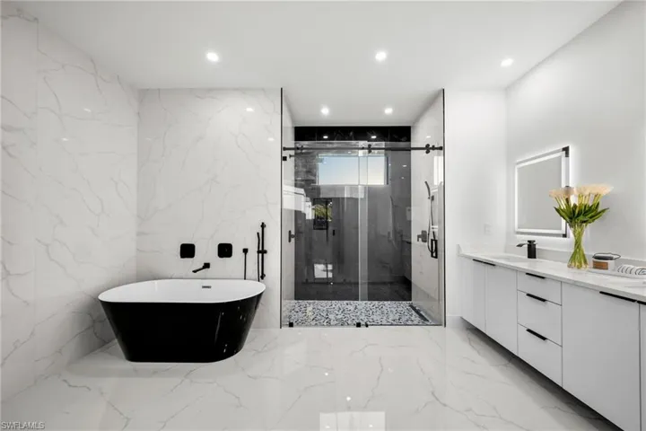 Bathroom with vanity, a marble finish shower, stone wall, a soaking tub, and marble finish floor