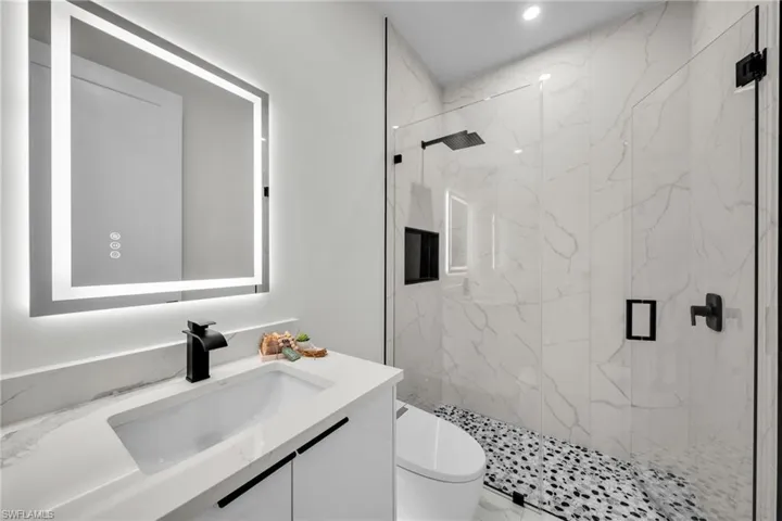 Bathroom with toilet, vanity, and a marble finish shower