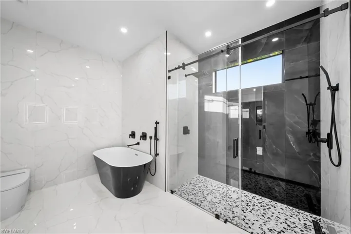 Bathroom with marble finish floor, stone wall, a marble finish shower, toilet, and a freestanding bath