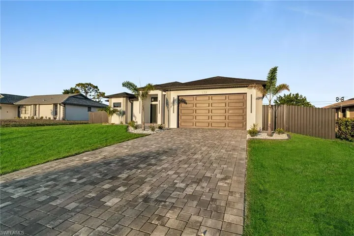 View of front of house featuring a front yard, stucco siding, an attached garage, fence, and decorative driveway