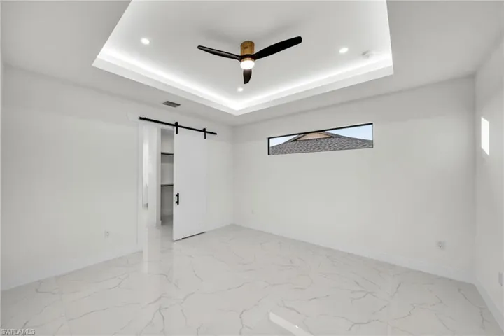 Unfurnished room with baseboards, a barn door, a tray ceiling, and recessed lighting