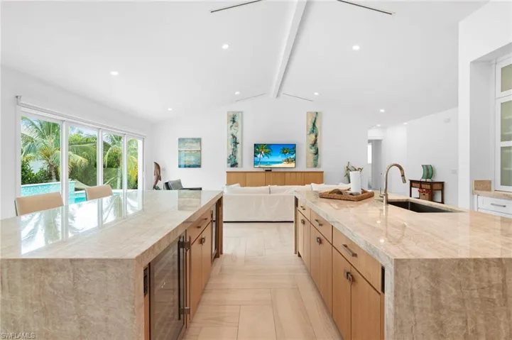 Kitchen with sink, light stone counters, a kitchen island with sink, light parquet floors, and beverage cooler