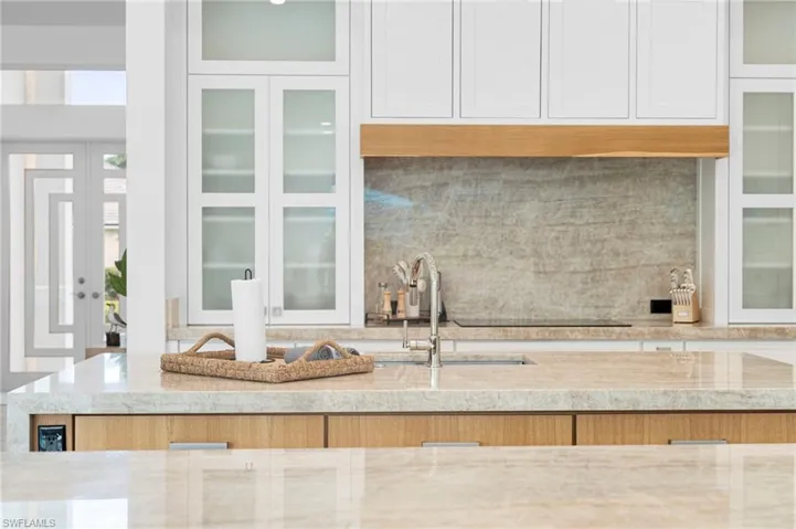 Kitchen featuring decorative backsplash, black electric cooktop, white cabinetry, sink, and light stone countertops