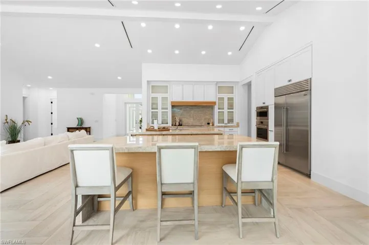 Kitchen with light parquet flooring, white cabinets, light stone countertops, stainless steel appliances, and lofted ceiling with beams