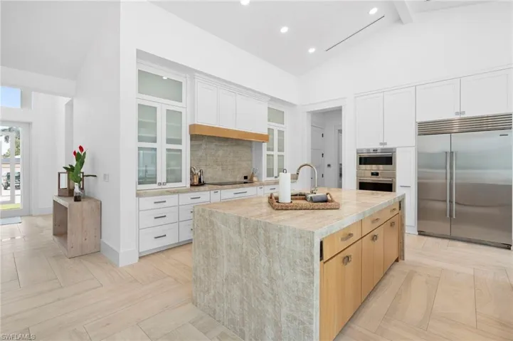 Kitchen with white cabinets, appliances with stainless steel finishes, an island with sink, and light parquet floors