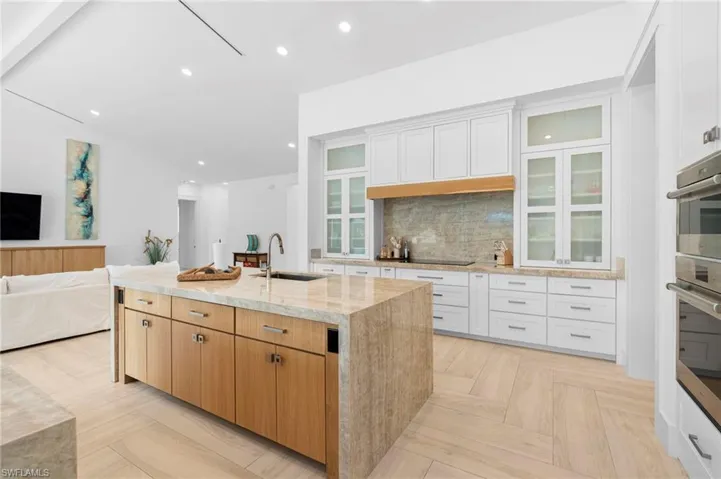 Kitchen featuring backsplash, sink, an island with sink, light parquet floors, and white cabinets