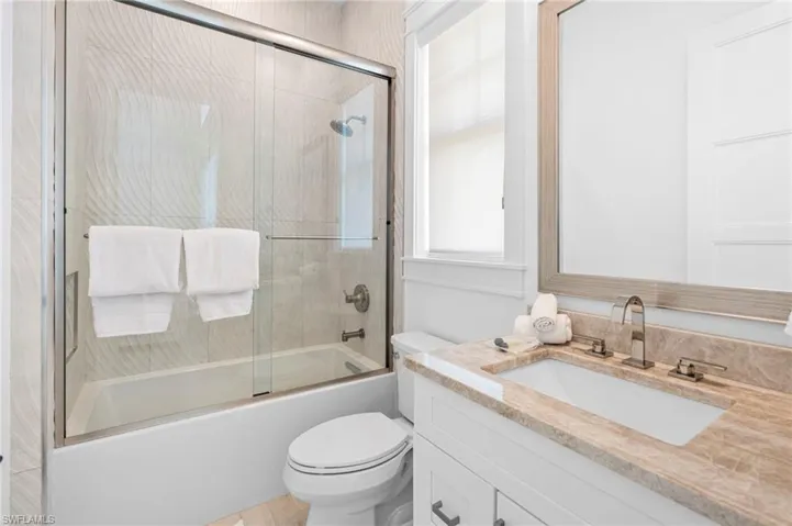 Full bathroom with enclosed tub / shower combo, vanity, and toilet