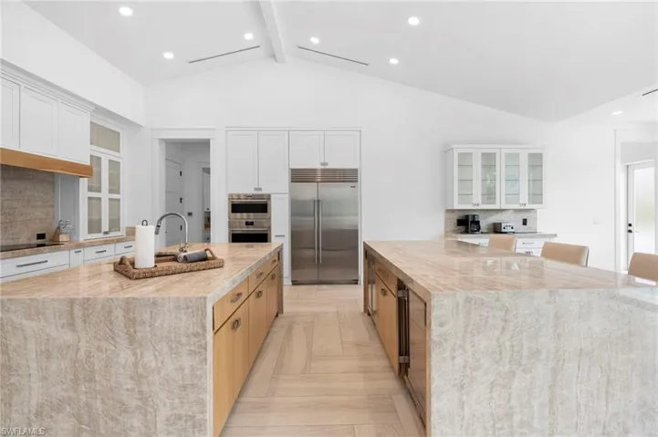Kitchen featuring backsplash, a large island with sink, appliances with stainless steel finishes, and light parquet floors