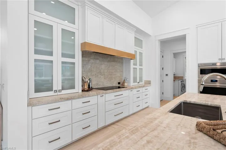 Kitchen featuring light wood-type flooring, white cabinetry, backsplash, and light stone counters