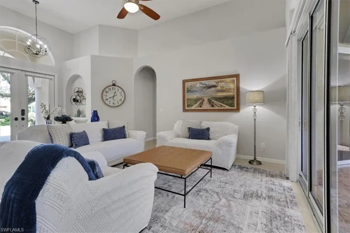 Living area featuring french doors, arched walkways, a ceiling fan, and a towering ceiling