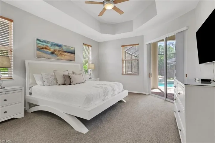 Bedroom with light colored carpet, a raised ceiling, access to outside, and multiple windows