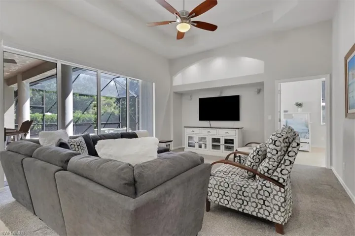 Living room featuring light colored carpet, a ceiling fan, a tray ceiling, a towering ceiling, and a sunroom