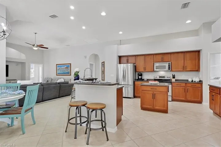Kitchen featuring a center island with sink, arched walkways, stainless steel appliances, ceiling fan, and brown cabinets