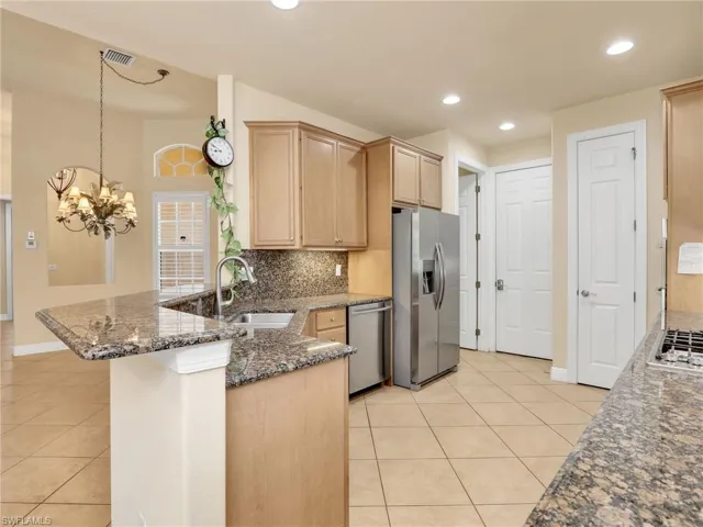 Kitchen with decorative backsplash, stainless steel appliances, dark stone countertops, light brown cabinetry, and decorative light fixtures