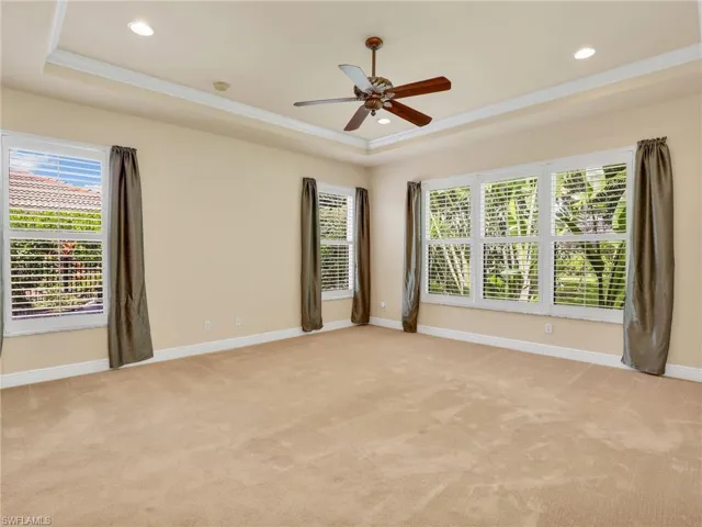 Unfurnished room featuring a raised ceiling, light colored carpet, ceiling fan, recessed lighting, and ornamental molding