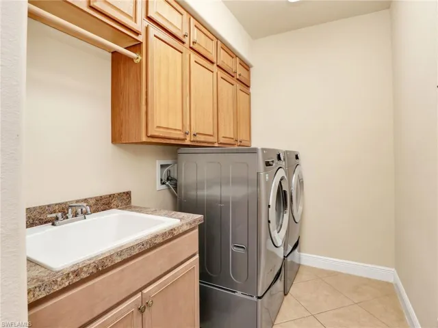 Laundry area featuring light tile patterned flooring, washing machine and clothes dryer, and cabinet space