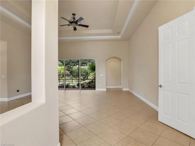 Unfurnished room with light tile patterned floors, arched walkways, a tray ceiling, and a ceiling fan