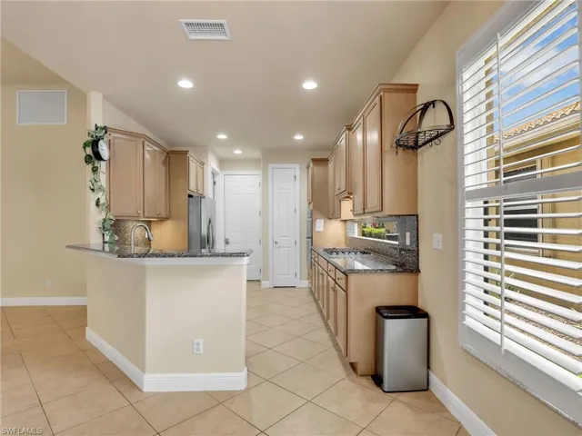 Kitchen featuring dark stone counters, light brown cabinetry, backsplash, recessed lighting, and a peninsula
