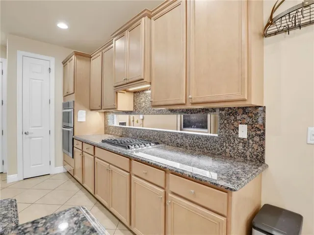 Kitchen with dark stone counters, tasteful backsplash, light brown cabinetry, light tile patterned flooring, and appliances with stainless steel finishes