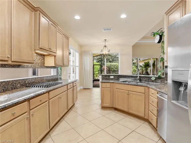Kitchen featuring stainless steel appliances, recessed lighting, light brown cabinets, dark stone countertops, and hanging light fixtures