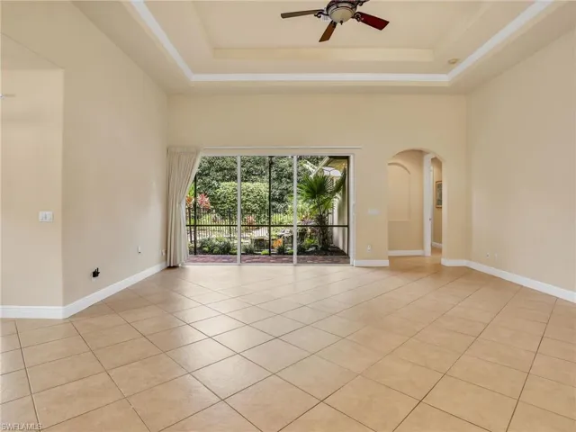 Unfurnished room featuring arched walkways, light tile patterned floors, a raised ceiling, and ceiling fan