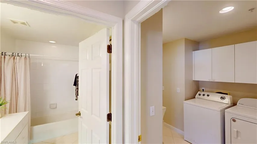 Washroom with cabinets, washing machine and clothes dryer, and light tile patterned flooring