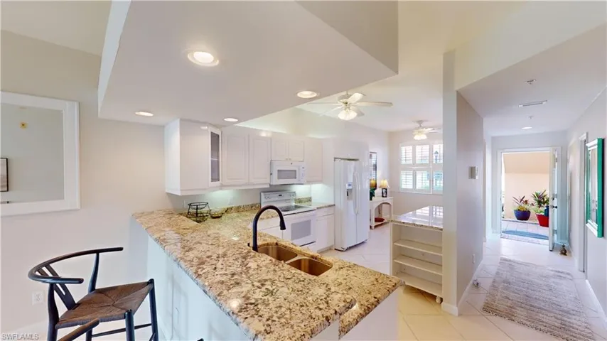 Kitchen featuring light stone counters, kitchen peninsula, a kitchen breakfast bar, white cabinetry, and white appliances