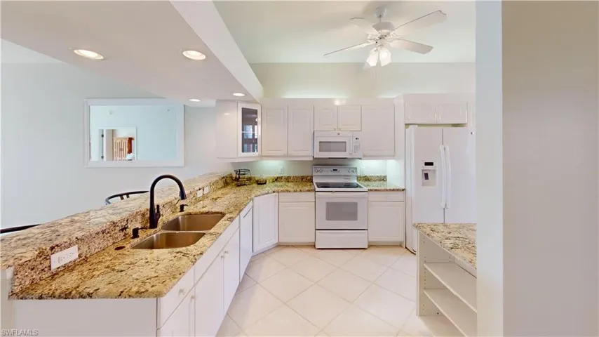 Kitchen with light stone counters, white cabinetry, white appliances, sink, and kitchen peninsula