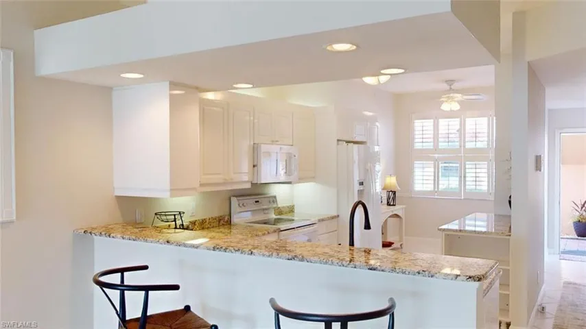 Kitchen with kitchen peninsula, light stone counters, and white appliances