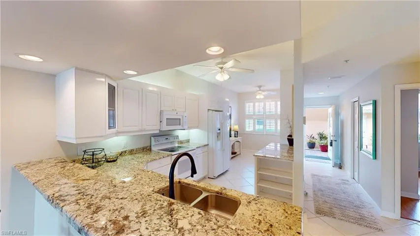 Kitchen with sink, light stone counters, kitchen peninsula, white appliances, and white cabinets