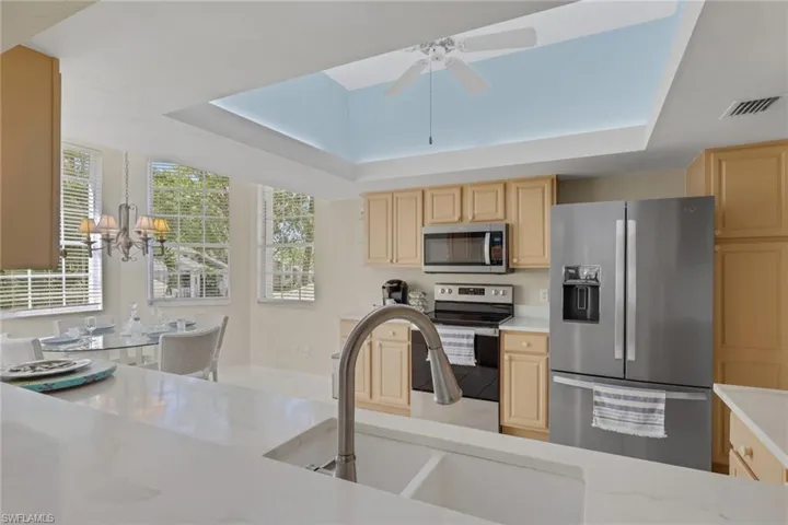 Kitchen featuring a tray ceiling, quartz counters,stainless steel appliances, a ceiling fan, light wood finish cabinets, and hanging lights