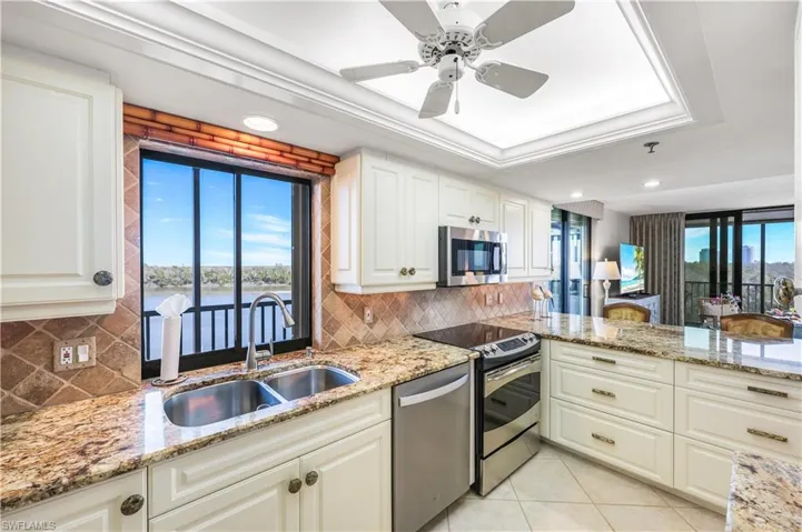 Kitchen with light stone counters, stainless steel appliances, a raised ceiling, white cabinets, and ceiling fan
