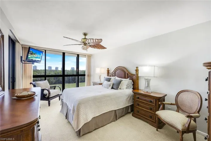 King bedroom with a wall of windows and ceiling fan and sliders open to lanai/patio
