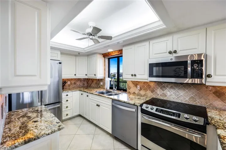 Kitchen with a tray ceiling, stainless steel appliances, white cabinetry, light stone counters, and custom molding