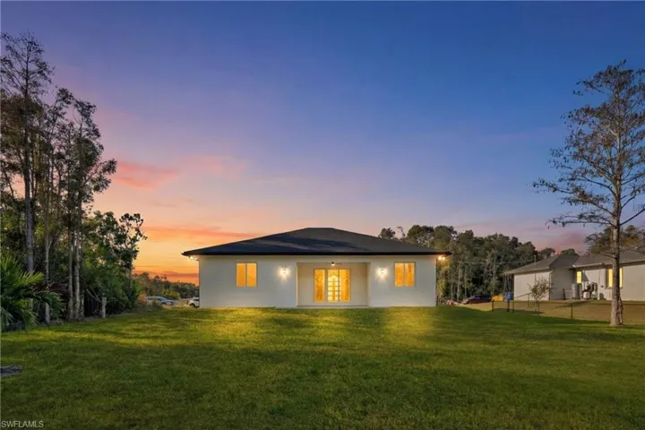 Back of house at dusk featuring a lawn, a patio area, and stucco siding