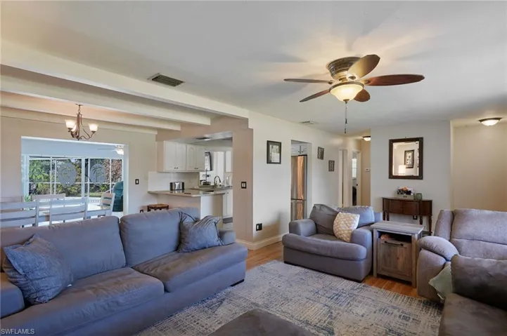 Living area with visible vents, baseboards, light wood-style floors, and ceiling fan with notable chandelier